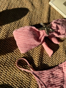 Detail of pink textured bikini top featuring a gold starfish charm and bow design