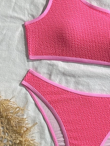 Detailed flat lay of bright pink seersucker bikini set with smooth trim on white fabric