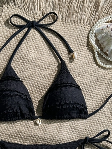 Detail of black bikini with ruffled texture and natural shell charms on straw mat