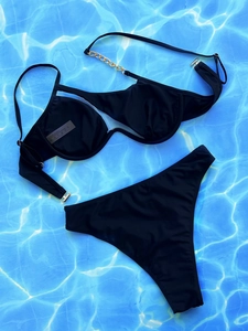 Detailansicht des schwarzen Bikinis mit Goldketten auf blauem Wasserhintergrund