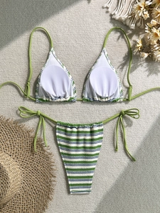 Detailed flat lay of green striped bikini set with beach accessories on woven mat