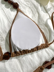 Brown crochet bikini top with beads and white padding on linen fabric background