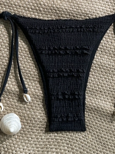 Detail of black ruched bikini bottoms with side ties and decorative white shells