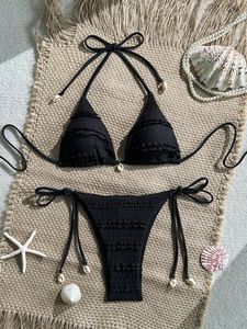 Detail of black textured bikini set with natural shell accents on beach woven mat