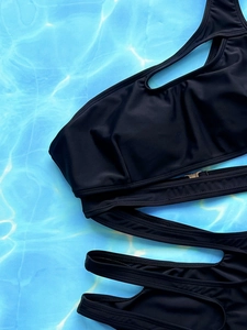 Flat lay of black one-shoulder bikini with cutout details on a blue pool water background