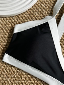 Detailed view of color-block bikini top with white contrast piping on black fabric
