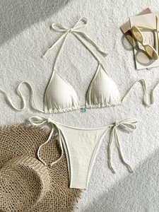 Detail of cream bikini with textured fabric and blue flower charm on white rug