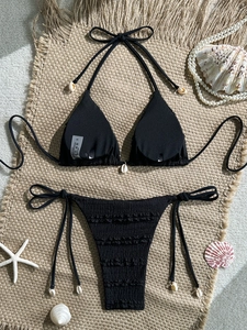 Detail of black bikini with textured frills and shell pendants on rustic mat