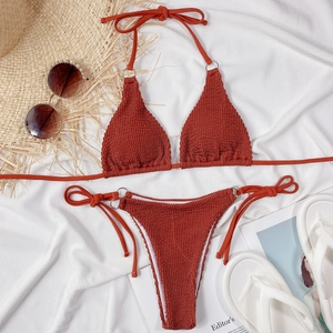 Flat lay of smocked rust red bikini set with metallic ring detail and beach accessories