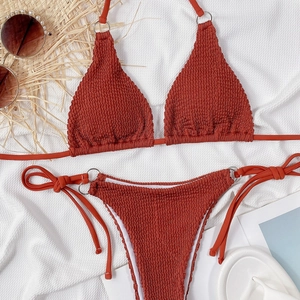 Flat lay of rust red textured bikini set with silver rings and summer beach accessories