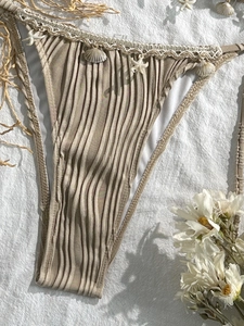 Detailed view of beige bikini bottom with vertical ribbing, lace trim and sea shell charms