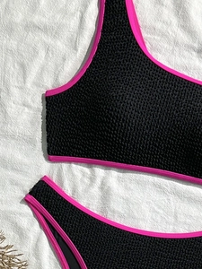 Two-piece black waffle textured bikini with neon pink trim and one-shoulder design