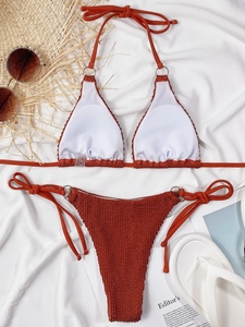 Flat lay of textured seersucker bikini in rust orange with metal ring details and accessories