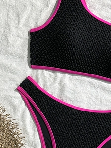 Two-piece black seersucker bikini with hot pink trim on a white fabric background