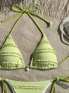 Detail of light green textured bikini set with ruffles and seashell decorations on sand mat