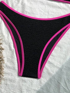 Black crinkle bikini bottom with pink neon trim on a natural linen background