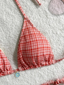 Macro detail of red and white gingham bikini top with a blue daisy charm pendant