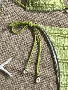 Close-up of light green textured bikini with seashell ties and delicate lace trim detail