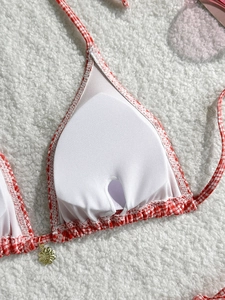 Detail of red gingham bikini top with built-in pads and gold flower charm on white texture