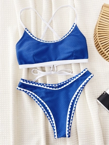 Detail of blue textured bikini with white wavy trim on a beige knitted background
