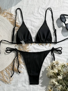 Flat lay of ribbed black bikini with decorative shells and starfish charms on white fabric