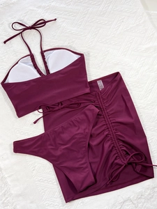 Detailed flat lay of a 3-piece burgundy bikini set with drawstring skirt on white textured rug