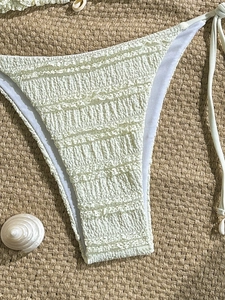 Solid cream textured bikini bottom with side ties and seashell charms on beach mat
