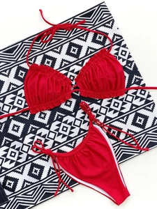 Flat lay of a red ribbed bikini set with halter top and tie-side bottoms on a patterned rug