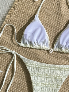 Three-piece beige textured bikini set with shell charms on a rustic straw mat background