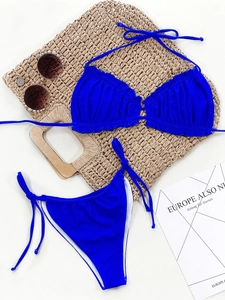 Flat lay of royal blue ruched bikini set with straw bag and pearl sunglasses