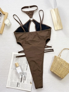 Deep brown cutout one-piece swimsuit with metal rings on a flat lay holiday setting