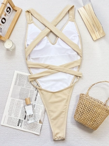Detail of cross-back straps and beige fabric on one-piece swimsuit with white lining