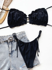 Flat lay of black ruffled bikini set with adjustable strings and denim shorts on white surface