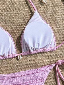 Detailed view of pink smocked bikini top with natural shell pendant on a woven mat