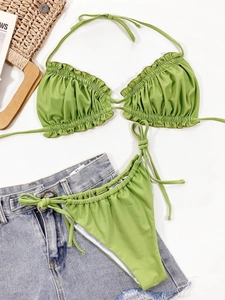Flat lay of lime green pleated bikini set with straw bag and denim shorts for vacation