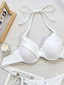 Flat lay of white ribbed bikini with ruffle edges and halter neck ties on beige fabric