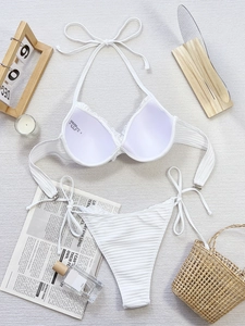 Flat lay of a white ribbed bikini set with neck tie and side-tie bottoms on a vacation set