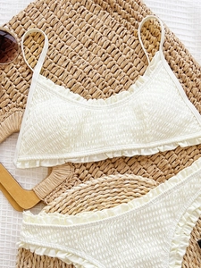Cream smocked two-piece bikini set with ruffle details on resort-style woven background