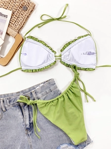 Flat lay of green bikini with ruffle details and summer holiday props on white background