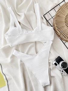 White ribbed two-piece bikini set with wide straps flat laid on resort themed background