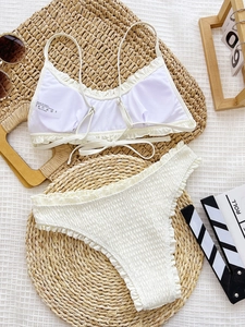 White smocked bikini set with tie straps and ruffled bottoms on a summer flat lay background