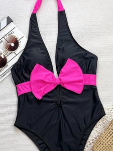 Detailed flat lay of black one-piece halter swimsuit with pink bow and vacation props
