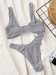 Flat lay of black and white gingham bikini set with vintage camera on a textured cloth