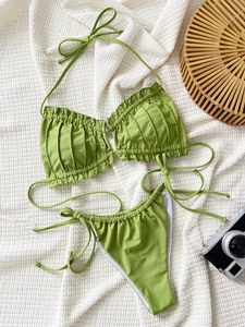Detailed view of olive green bikini with ruffled texture and side ties on beach fabric
