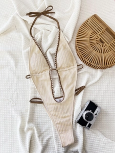 Detail of V-neck one-piece swimsuit with contrast piping and side tie strings on white fabric