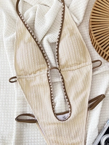 Detail of crinkled one-piece swimsuit with scalloped trim and brown piping details