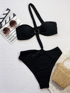 Flat lay of ribbed black monokini with side cutouts and silver ring detail on white texture