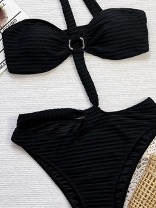 Detail of black ribbed monokini with silver metal ring and halter neck tie on plush background