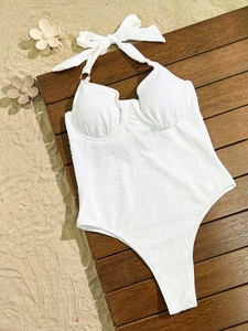 Detailed top view of white one-piece bikini with floral jacquard texture on wood surface