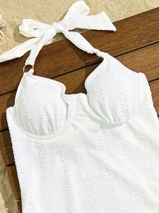 Close-up of white jacquard fabric swimsuit with golden ring and halter neck detail